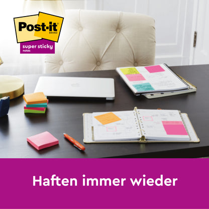 Ein Schreibtisch mit gestapelten Post-it® Super Sticky Z-Notes Boost Collection (76x76mm, 90 Blatt/Block, 100% PEFC) von 3M Deutschland GmbH, einem offenen Planer mit bunten Notizen, einem Stift, einem geschlossenen Laptop und einer Lampe. Text: "Haften immer wieder." Logo oben links.