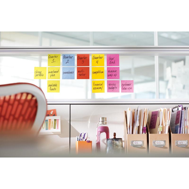 En kontorscene med Post-it® Super Sticky Notes (76 mm x 76 mm, 90 ark/blok, PEFC) fra 3M Deutschland GmbH, farverigt arrangeret på en glasvæg til kvartalsopgaver. Foran: mapper, dokumenter, en lyserød flaske og en rød stol.