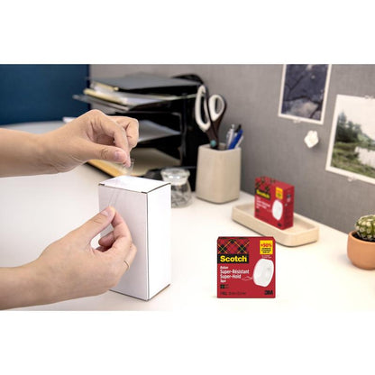 En person forsegler en hvid æske med kontorartikler med Scotch® Super-Hold Secure Tape, 1 rulle, 19 mm x 25,4 m fra 3M Deutschland GmbH. Emballagen til tapen er indsat i nederste højre hjørne.