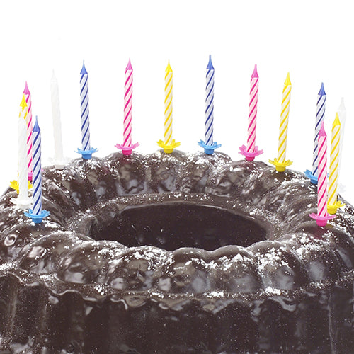 En chokoladekage drysset med flormelis og dekoreret med ti PAPSTAR fødselsdagslys 6 cm, farvesorteret med holder (fra PAPSTAR GmbH) i forskellige farver.