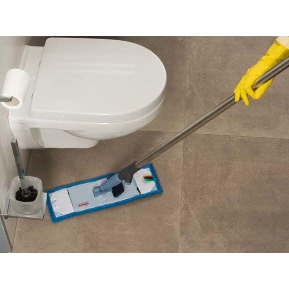 En person med gule handsker tørrer effektivt det flisebelagte badeværelsesgulv ved siden af et hvidt toilet med Vileda Professional SprayPro rustfrit stål moppeholder fra Vileda GmbH, der er udstyret med en blåkantet pude. I nærheden er der en holder, hvor toiletbørsten opbevares.