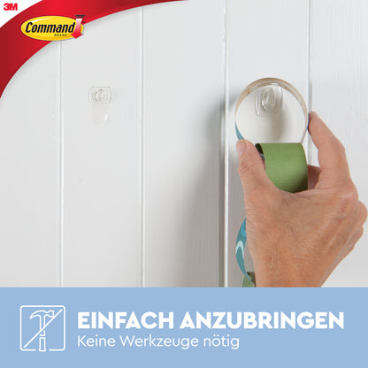 Eine Hand befestigt einen Command™ Mini-Haken, transparent, von 3M Deutschland GmbH an einer weißen Holzwand. Text: "Einfach anzubringen. Keine Werkzeuge nötig. Spurlos entfernen mit transparenten Strips (17006CLR).