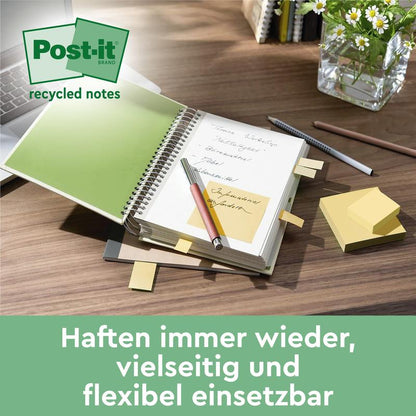 En spiralnotesbog med Post-it® genbrugssedler (38 mm x 51 mm, 100 ark/blok, 100% PEFC, fra 3M Deutschland GmbH) ligger åben på et skrivebord ved siden af en pen, en lukket notesbog, klistermærkeblokke og en glasbeholder med grønne planter. Tysk tekst nedenfor.