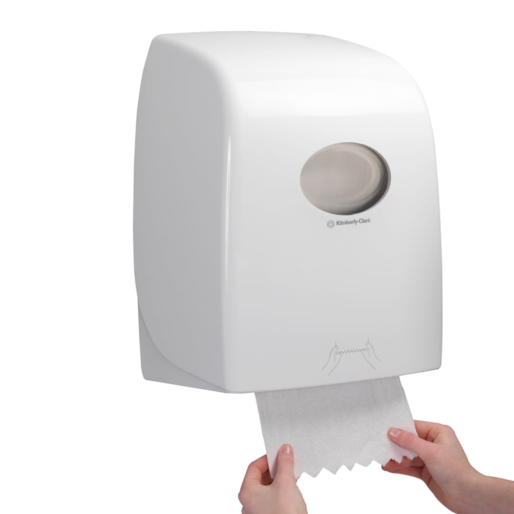 Nogen trækker et ark Scott® ESSENTIAL™ Håndklæder - Rulle fra en hvid, vægmonteret dispenser fra Kimberly-Clark GmbH, hvis gennemsigtige vindue giver udsigt til håndklæderullerne indeni.