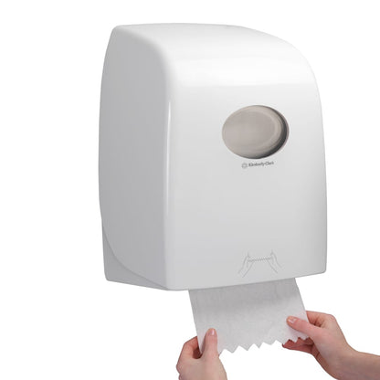 Nogen trækker et ark Scott® ESSENTIAL™ Håndklæder - Rulle fra en hvid, vægmonteret dispenser fra Kimberly-Clark GmbH, hvis gennemsigtige vindue giver udsigt til håndklæderullerne indeni.