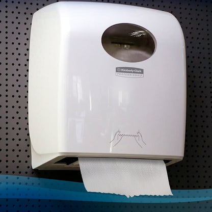 En vægmonteret hvid Kimberly-Clark GmbH Scott® Control™ Slimroll™-dispenser rummer synlige papirhåndklæder og har et gennemsigtigt vindue og en vejledning til håndtørring på forsiden; installeret på en perforeret væg (6 ruller/kasse, hvid).