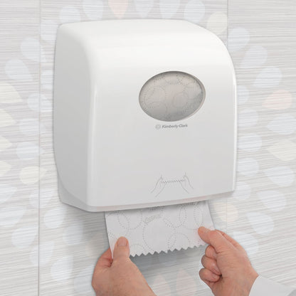 Nogen trækker et Kleenex® Ultra™ Slimroll™ håndklæde fra en hvid, vægmonteret dispenser med vindue og symboler i et flisebelagt toilet. Produkt: 6-rulle-kasse fra Kimberly-Clark GmbH.