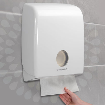 En hånd trækker et Kleenex® Ultra™ håndklæde ud af en vægmonteret hvid dispenser fra Kimberly-Clark GmbH, installeret på en flisevæg (Interfold/Hvid/Stor - 30 clips x 94 ark | karton, 30 pakker).