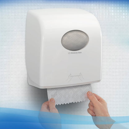 En person trækker Scott® CONTROL EXTRA STRONG håndklæder ud af en vægmonteret, hvid dispenser fra Kimberly-Clark GmbH, der står på hvide, strukturerede fliser. På forsiden af rullehåndklædedispenseren er en enkel brugsanvisning afbildet.