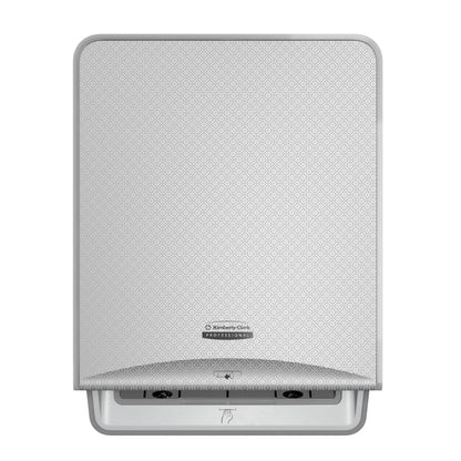 En sølvfarvet mosaik, vægmonteret Kimberly-Clark Professional™ Icon™ elektronisk No Touch-Løse Modul-Rulle fra Kimberly-Clark GmbH med en mønstret frontplade, centralt logo og en åbning i bunden til berøringsfri håndklædeudlevering.