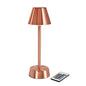 Den trådløse LED-lampe ZELDA i rosaguld fra Duni GmbH har en konisk skærm, en cylindrisk sokkel og leveres med en lille fjernbetjening med farverige knapper.