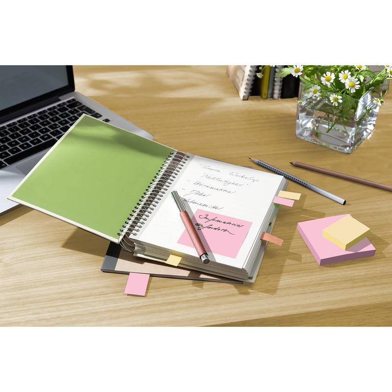 En spiralnotesbog med håndskrevne noter, en pen, en bærbar computer, en blyant og Post-it® genbrugssedler (38x51mm, 100 ark/blok, 100% PEFC) fra 3M Deutschland GmbH på et skrivebord; i baggrunden en glasvase med hvide margueritter.