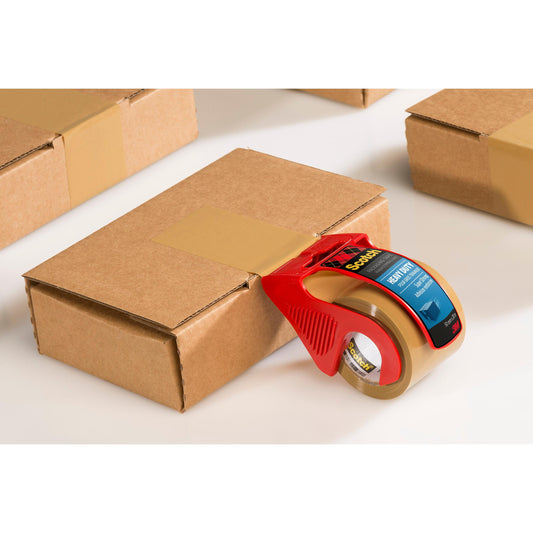 Ein Scotch® Extra starkes Verpackungsklebeband, Braun (48 mm x 20,3 m) von 3M Deutschland GmbH im roten Handabroller verschließt einen Karton; weitere versiegelte Boxen liegen daneben auf weißem Untergrund.