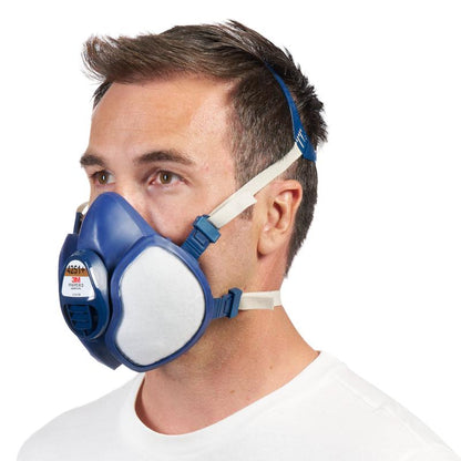 En mand i profil bærer 3M™ åndedrætsmaske med integrerede filtre fra 3M Deutschland GmbH i farverne blå og hvid med justerbare hovedbånd foran en enkel hvid baggrund.
