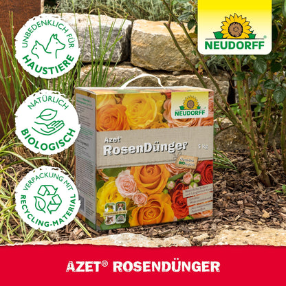 En kasse Neudorff Shop Azet RosenGødning ligger i en have mellem sten og planter. Emballagen understreger sikkerheden for kæledyr, naturlige ingredienser og genanvendelige materialer til blomstrende roser.