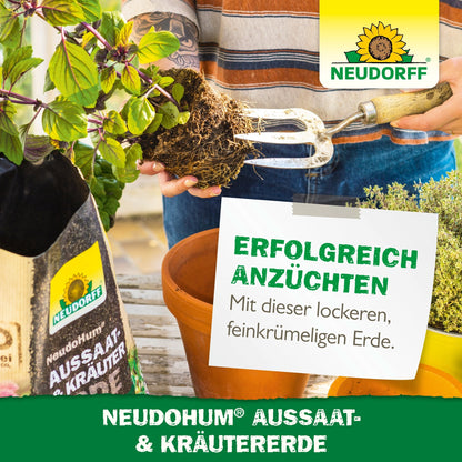 En person bruger en havegaffel til at forberede jorden i en rektangulær plantebeholder. Ved siden af står en pose med NeudoHum Så- & Krydderurtejord fra Neudorff Shop med middelhavskrydderurter, krydderurteplanter, branding og tysk reklametext.