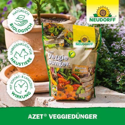 En pose Neudorff Shop Azet VeggieGødning står på en træoverflade udendørs ved siden af en terrakottakrukke med grønne planter. På emballagen er der grøntsagsbilleder og certificeringslogoer.