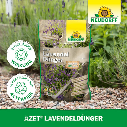 En pose Neudorff Shop Azet LavendelGødning ligger på en havegang af grus ved siden af lavendel med blå-violette blomster. På emballagen står der "miljøvenlig" på tysk.
