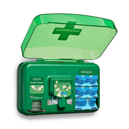 En blå sårplejedispenser fra Orkla Wound Care AB er åben og giver udsigt til sårrensepakker, plaster og en rulle bløde skumbind, der er arrangeret i individuelle rum.