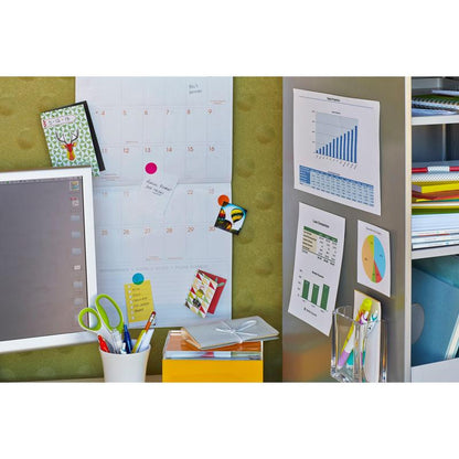 Et arbejdsområde med en vægkalender, tabeller fastgjort med 3M Scotch-FIX™ Aftagelige Monteringsfirkanter 108-ST64-P, en computerskærm, farverige mapper, en saks i en hvid holder, en gul kasse og et glas med penne. Noter er hæftet med disse klæbepuder uden rester.