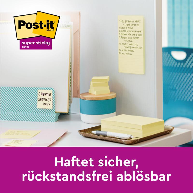 På et skrivebord er der Post-it® Super Sticky Notes (76 mm x 127 mm, 90 ark/blok, 100% PEFC) fra 3M Deutschland GmbH på en væg og på en overflade, mærkede mapper "Creative Services Kit" og kontorartikler. Teksten lyder: "Sidder sikkert, kan fjernes uden rester.