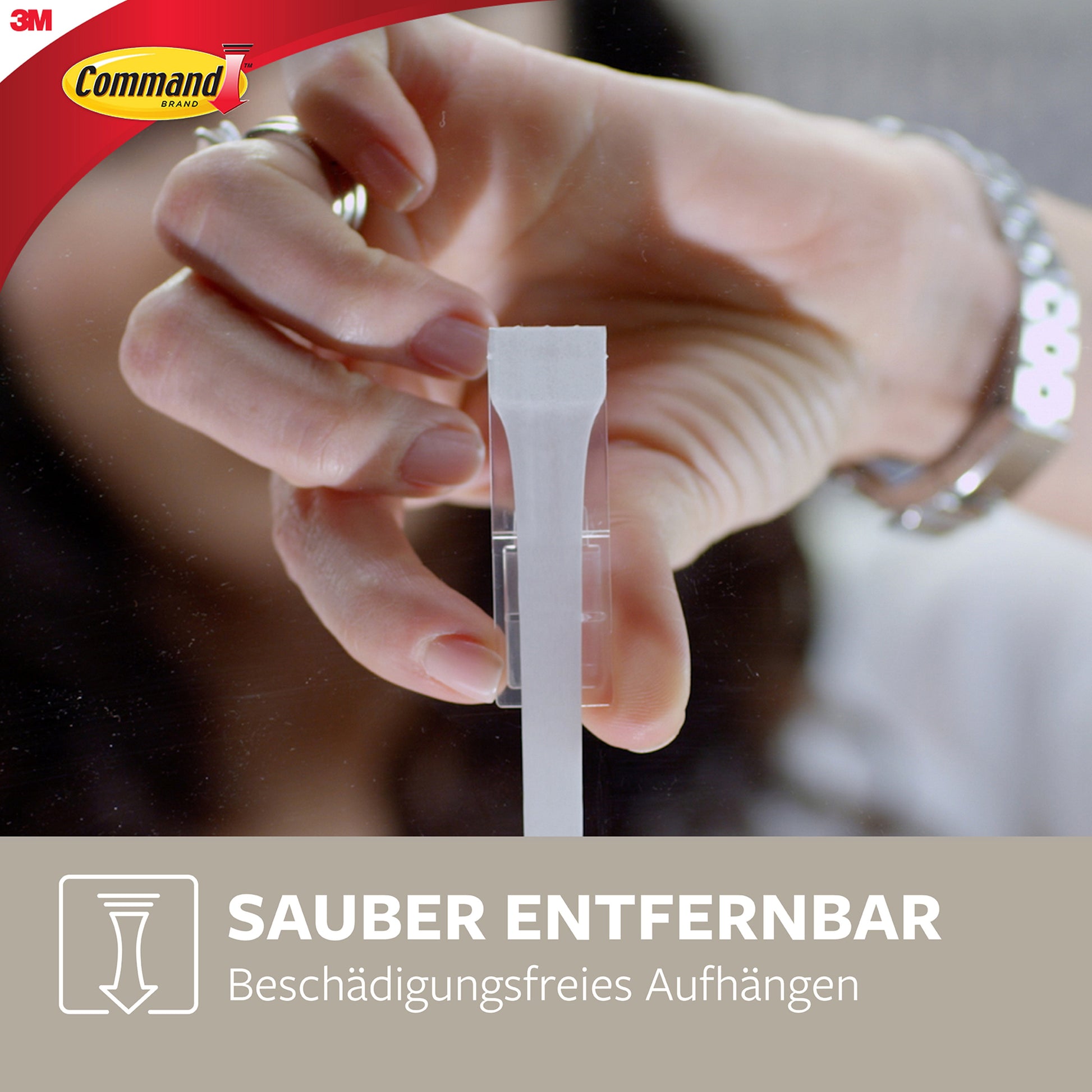 Eine Hand zieht den Klebestreifen eines mittelgroßen Command™ Metallhakens in gebürstetem Nickel, 17034 (1 Haken, 2 Strips) von 3M Deutschland GmbH von einer Glasscheibe. Text: "Sauber entfernbar - Haken ohne Bohren." Command & 3M Logos sichtbar.