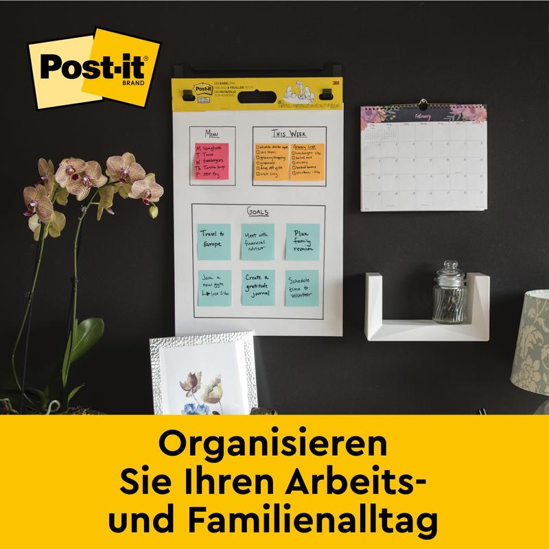 En kontorvæg med Post-it® Super Sticky selvklæbende mødeplanchart/flipchart 559 fra 3M Deutschland GmbH (63,5 x 76,2 cm), månedskalender, hylde med glas, orkidé og fotos. Tekst: "Organiser din hverdag.