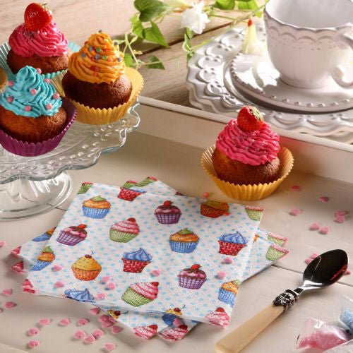 Et bord er dækket med cupcakes på et glasstativ, en tallerken, ske, hvid tekop og underkop, lyserøde hjerteformede drys og farverige PAPSTAR 20 servietter 33x33cm 3-lags 1/4-fals design sæt 5 fra PAPSTAR GmbH.