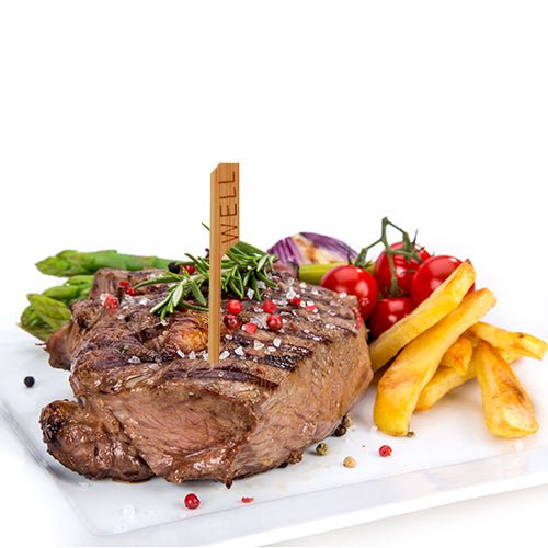 En grillet bøf med inskriptionen "WELL" og en PAPSTAR 250 Steak-markør (9 cm, PAPSTAR GmbH) serveres på en hvid tallerken med asparges, cherrytomater, ristede løg og pommes frites, garneret med rosmarin og peberkorn.
