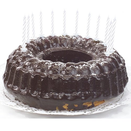En chokoladekage med skinnende glasur, dekoreret med PAPSTAR GmbH fødselsdagslys 6 cm, hvid med holder (24 stykker), jævnt fordelt langs kanten og ligger på en hvid blonde serviet.