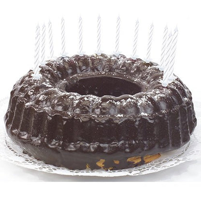 En chokoladekage med skinnende glasur, dekoreret med PAPSTAR GmbH fødselsdagslys 6 cm, hvid med holder (24 stykker), jævnt fordelt langs kanten og ligger på en hvid blonde serviet.