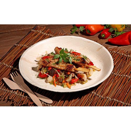 Grillet kødspyd med blandede grøntsager og krydderurter serveres på en PAPSTAR 25 tallerken, palmeblad "pure" rund fra PAPSTAR GmbH, med miljøvenligt engangsservice og farverige peberfrugter og grøntsager i baggrunden.