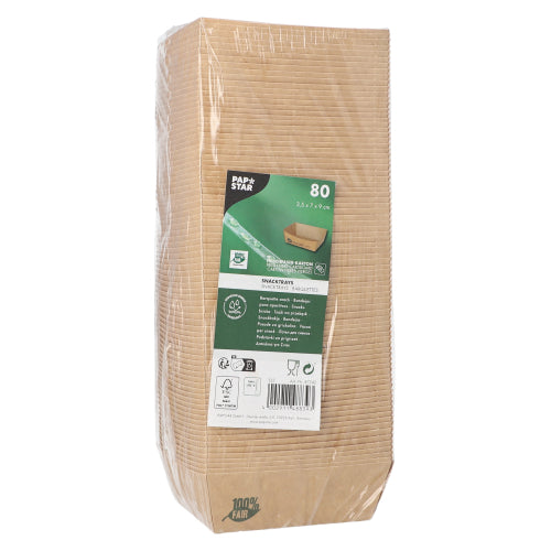 En pakket pakke med 80 PAPSTAR snackbakker "pure" brun "100% Fair" fra PAPSTAR GmbH står oprejst, med en etiket på forsiden, der viser produktdetaljer samt symboler for miljøvenlighed og biologisk nedbrydelighed; den gennemsigtige pakning giver udsigt til stablede bakker indeni.