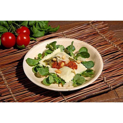 En tallerken ravioli med pesto, soltørret tomatsauce, pinjekerner og ost serveres på friskt grønt i en PAPSTAR palmebladsskål (17,5 cm), en miljøvenlig skål fra det 6-delte sæt fra PAPSTAR GmbH, serveret med tomater og bladgrøntsager i baggrunden.