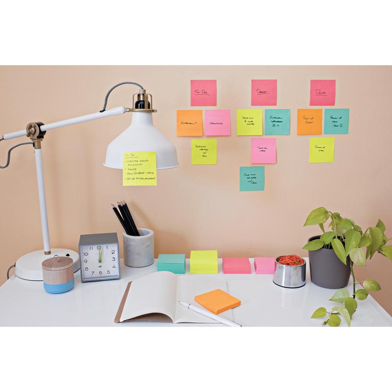 På det ryddelige skrivebord står en lampe, et ur, en plante, skriveredskaber og en åben notesbog. Ovenover viser farverige 3M Deutschland GmbH Post-it® Super Sticky Notes (76 mm x 127 mm, 90 ark/blok) håndskrevne opgaver og påmindelser på væggen.