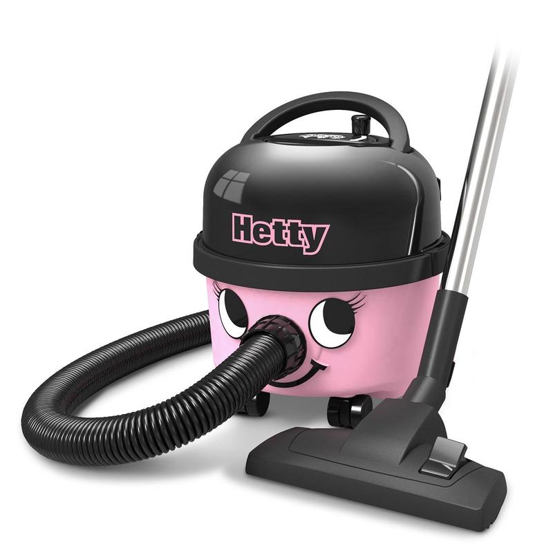 Den Hetty Compact støvsuger HET160-11 fra Numatic International GmbH er en lyserød-sort beholderstøvsuger med et smilende ansigt, en fleksibel slange, en mobil base og et sugehoved, der står ved siden af enheden på gulvet.