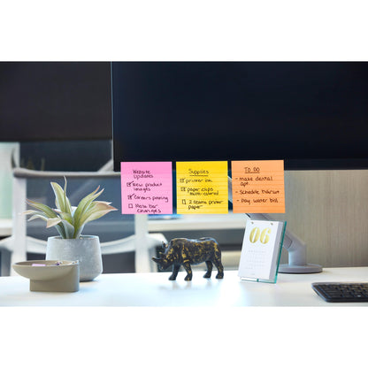 Ein Computermonitor zeigt bunte Post-it® Super Sticky Notes im Großformat (101 mm x 101 mm, 90 Blatt/Block, 100% PEFC) von 3M Deutschland GmbH mit Website-Updates, Material und Aufgaben. Auf dem Schreibtisch stehen eine Pflanze, eine schwarze Elefantenfigur und ein Tischkalender mit der Jahreszahl "06".