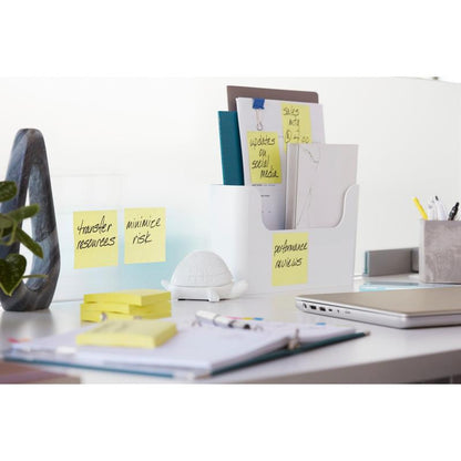 Et ryddeligt kontorbord med Post-it® Super Sticky Notes (76x127 mm, 90 ark, 100% PEFC) fra 3M Deutschland GmbH på en glasadskiller, dertil mapper i en holder, en skildpaddefigur, kontorartikler, en lukket bærbar computer og en åben notesbog med pen.