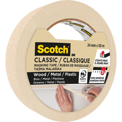 En rulle 3M Scotch® Classic afdækningstape, 24 mm x 50 m, 70% PEFC (SGSCH-COC-110078), ideel til maler- og renoveringsarbejde på træ, metal, plastik. Den høje klæbeevne holder op til to dage. Billedet viser en hånd, der sætter tapen på.