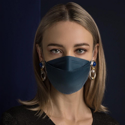 Eine Person mit langen Haaren trägt eine Altruan Designer Gesichtsmaske Partikelfiltrierend in Blau, die wirksamen Schutz nach FFP2-Standard bietet. Sie kombiniert sie mit großen dekorativen Ohrringen vor einem dunklen Hintergrund und trägt ein schwarzes Hemd.