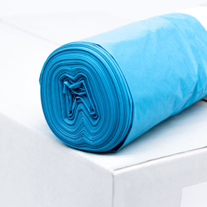 En rulle blå DEISS LDPE affaldssæk Type 60, 20772, 70 liter fra EMIL DEISS KG (GmbH + Co.) ligger på en hvid kasse. Disse holdbare sække, kendt for deres rivestyrke, er pænt rullet for at gøre lagstrukturen af genbrugsmaterialet synlig. Baggrunden forbliver enkel og minimalistisk.