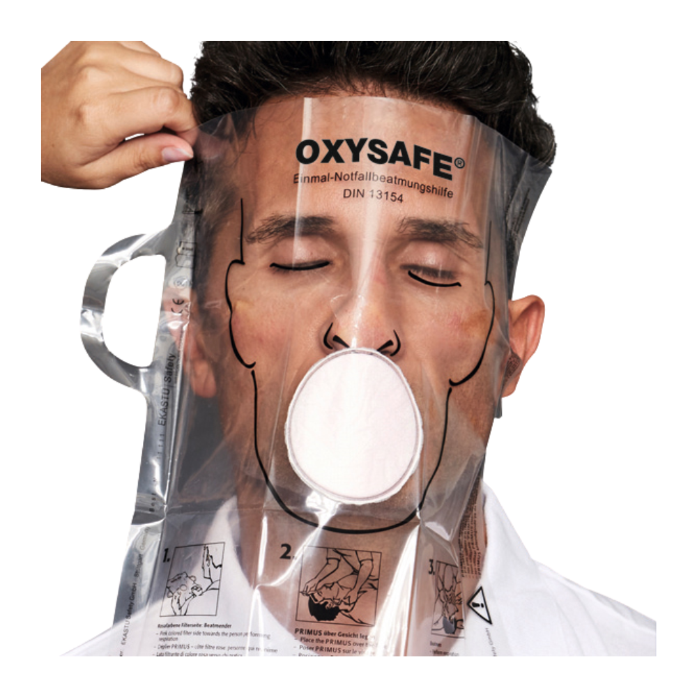 En person bærer en transparent Holthaus Oxysafe® nødhjælpsmaske fra Holthaus Medical GmbH & Co. KG og har lukkede øjne, mens en anden person justerer masken. Produktet er forsynet med instruktioner og diagrammer, der er trykt på plastoverfladen.