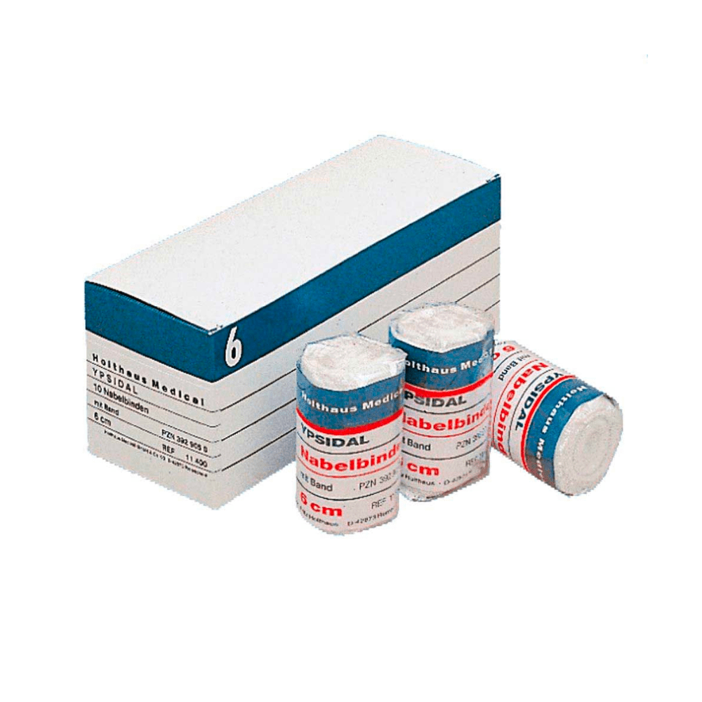 I en hvid papkasse med påskriften »Holthaus YPSIDAL navlebandage« og blå og hvide striber ligger en rulle med en medicinsk bandage på 6 cm x 2 m, der er fremstillet af 100 % bomuld. Foran papkassen ligger tre ruller elastisk bandage af mærket »Mollelast Medical« med påskriften »8 cm«.