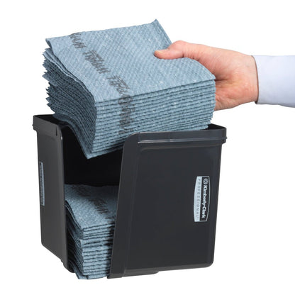 En hånd lægger kvartfoldede klude i den grå Kimberly-Clark Professional™ kluddispenser fra Kimberly-Clark GmbH - for hygiejnisk klududtagning. De pænt foldede klude og den forreste etiket er synlige.