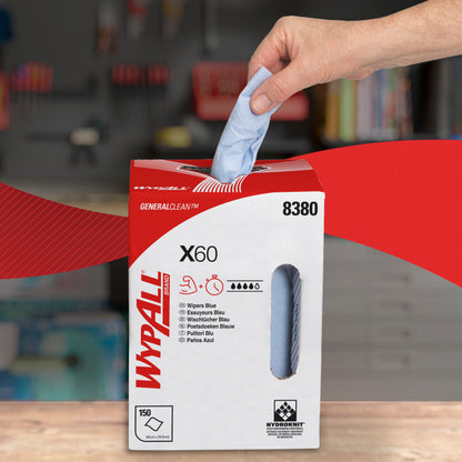 Eine Hand zieht ein blaues WypAll® X60 General Clean Blatt aus einem weiß-roten Spenderkarton der Kimberly-Clark GmbH mit der Aufschrift "8380", "150 Blatt" und "Zentralentnahme". Im Hintergrund ist eine unscharfe Werkstatt mit Regalen zu sehen.