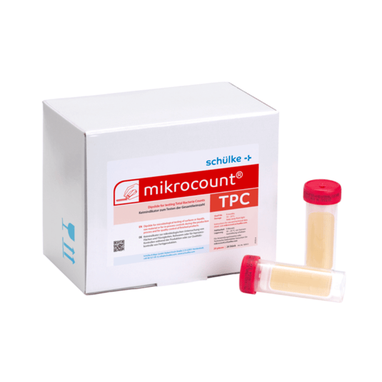 En hvid æske med påskriften »Schülke & Mayr GmbH Mikrocount® TPC, næringsmedium | Pakke (20 stk.)« med et logo og en produktbeskrivelse ved siden af to små flasker til mikrobielle tests, den ene med et gult låg, den anden med et gennemsigtigt låg.