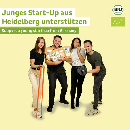 Vier junge Erwachsene lächeln vor einem hellgelben Hintergrund und halten Fairnatural® Bio Veganes Proteinpulver Kokos ohne Soja-Packungen. Der Text darüber wirbt um Unterstützung für ein Heidelberger Start-up-Unternehmen. Sichtbar sind die Logos der Bio-Zertifizierung.