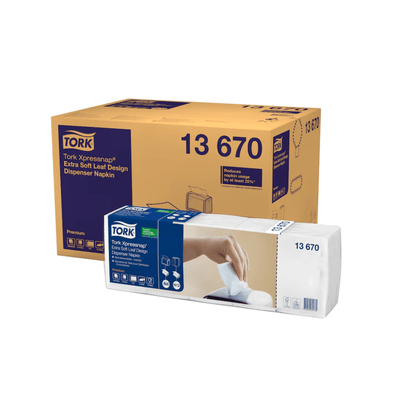 En Tork Xpressnap® 13670 dispenser servietboks i ekstra blødt bladdesign med mærket TORK fra Essity Professional Hygiene Germany GmbH vises ved siden af en pakke, hvor en hånd trækker en serviet ud af dispenseren.