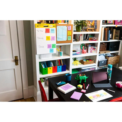 I et hjemmekontor står et sort bord med skriveredskaber, en tablet og notesbøger. I baggrunden er der hylder med bøger og mapper samt en opgaveliste på et whiteboard med 3M Post-it® Super Sticky Notes (76x127 mm, 90 ark/blok, 100% PEFC).