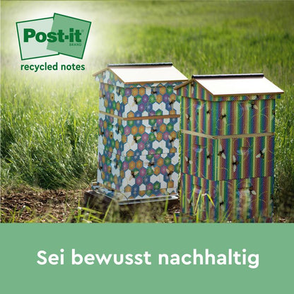 To farverige bistader med sekskantede mønstre står på en eng i sollyset. I hjørnet står logoet for Post-it® genbrugssedler, 38 mm x 51 mm, 100 ark/blok, 100% PEFC af 3M Deutschland GmbH. Teksten nedenfor lyder: "Vær bevidst bæredygtig.